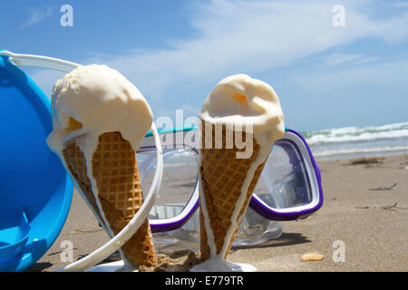 Vanilla ice cream cones melting on a summer beach with goggles and sand pail Stock Photo