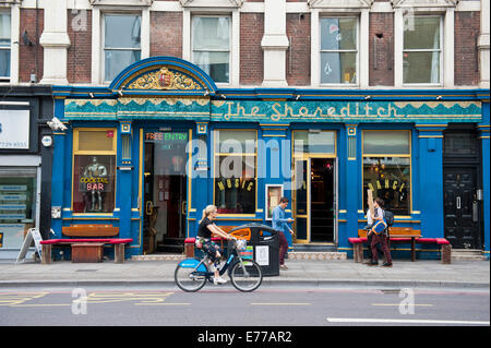 The Shoreditch, bar, restaurant and music venue in the East End of London, with a girl on a 'boris bike' driving past. Stock Photo