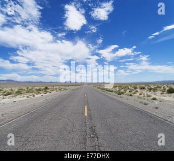an empty desert road cuts across Nevada to the horizon under a partly cloudy blue sky