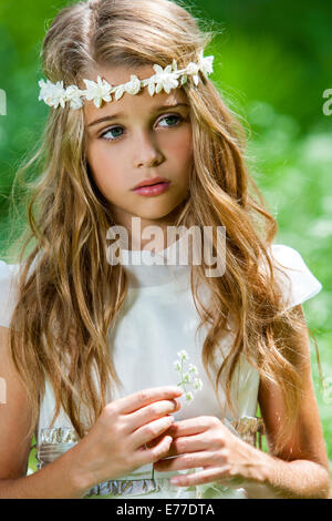 Close up portrait of cute girl in white dress holding flower outdoors. Stock Photo