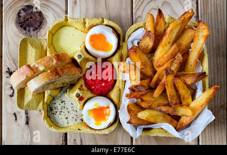 Two soft boiled eggs with french fries and sauces in a crate cardboard box. Stock Photo