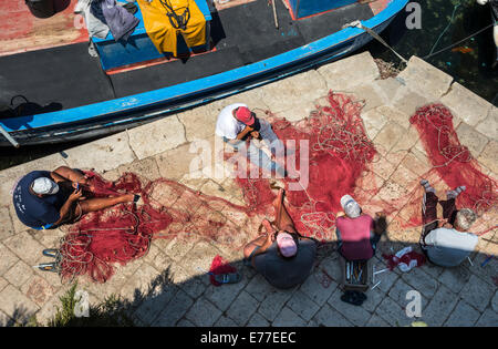 Fishermen mending  fishing nets on the quay in the old town of Gallipoli, Puglia, Southern Italy. Stock Photo