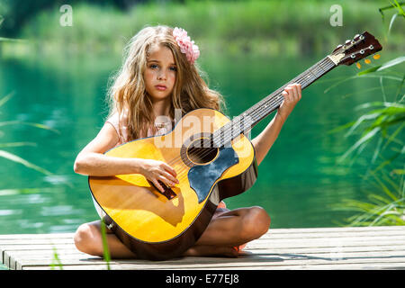 Portrait of young girl playing guitar on river jetty. Stock Photo