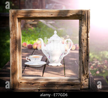 Vintage picture of tea set in garden in wooden frame. Stock Photo