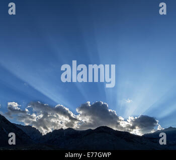 sunrays across a blue sky from behind a cloud over the Sierra Nevada Mountains and Taboose Pass Stock Photo