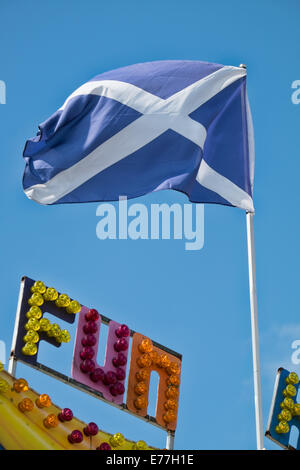 The Saltire, the Scottish national flag flying atop a flagpole above the word fun written in multi coloured  fairground lights Stock Photo