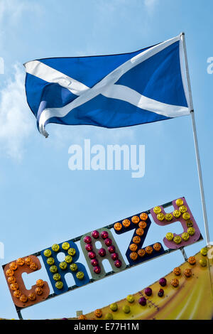 The Saltire, the Scottish national flag flying atop a flagpole above the word crazy written in multi coloured  fairground lights Stock Photo