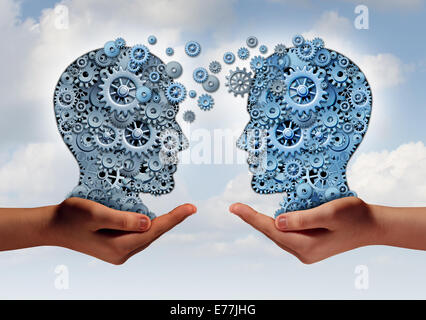 Business technology concept as two hands holding a group of  machine gears shaped as a human head as a symbol and metaphor for the transfer of industry information or corporate training. Stock Photo