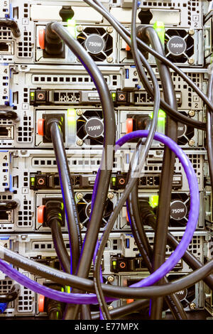 Tangle of power and ethernet cables plugged into the back of a computer server machine at a data center Stock Photo