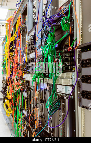 Tangled mess of fiber and ethernet cables plugged into router machines at computer data center supporting cloud computing Stock Photo
