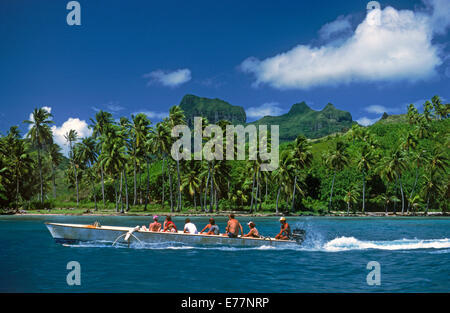 Outrigger canoe with tourists motoring past Island of Bora Bora in French Polynesia Stock Photo