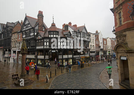 Historic English city of Chester with shoppers in pedestrian mall passing iconic black & white 14th century buildings, The Rows Stock Photo