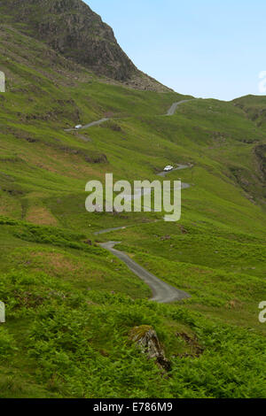 View of steep narrow road leading to summit of Hardknott Pass in Cumbria winding through English landscape of green cloaked treeless mountains Stock Photo