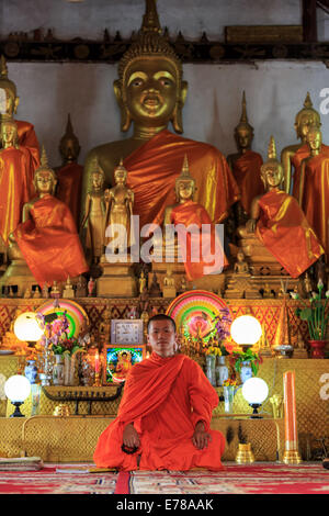 A monk meditating in the lotus position in front of golden Buddhas Stock Photo