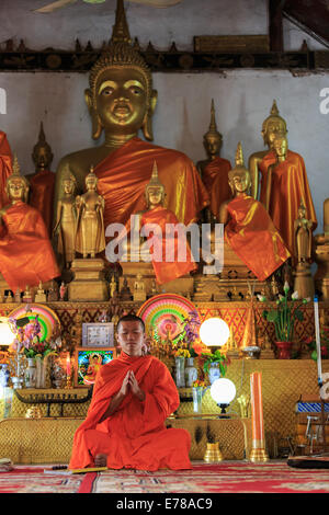 A monk praying in front of golden Buddhas, vertical Stock Photo