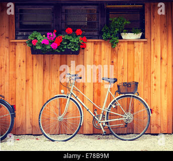 Bicycle parked near a wooden cabin with geranium and herbs vases. Retro Instagram-like effect added. Stock Photo