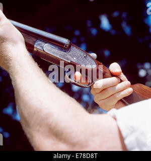 A double barreled Shotgun is pointed into the air with the operator using his finger to pull the trigger. Stock Photo