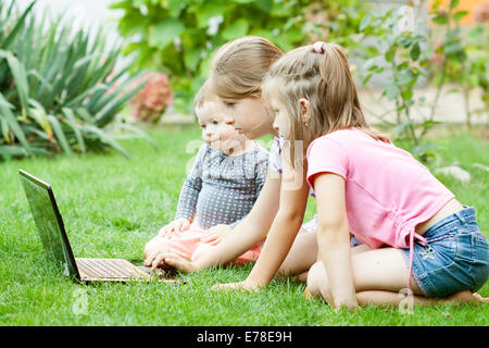 Curious kids with laptop computer laying in the grass Stock Photo