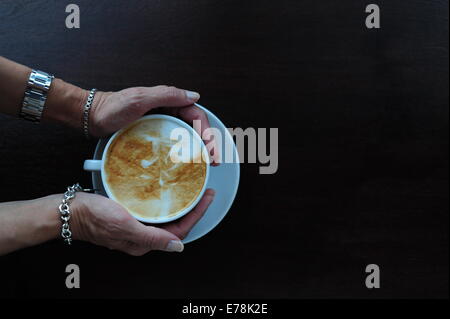 Mature woman in cafe holding a cup of coffee cappuccino over head view Stock Photo