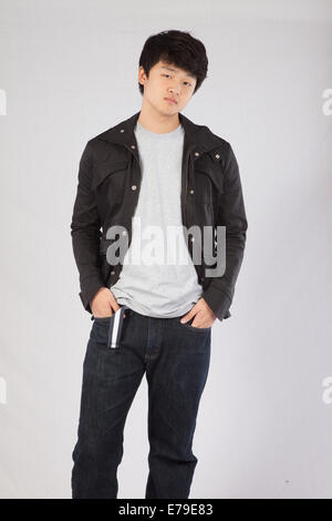 Handsome Asian man in a jacket and looking thoughtful with his hands in his pockets Stock Photo