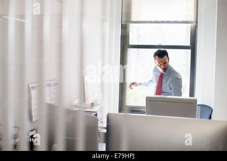 A man standing over a desk looking at a computer screen. Stock Photo