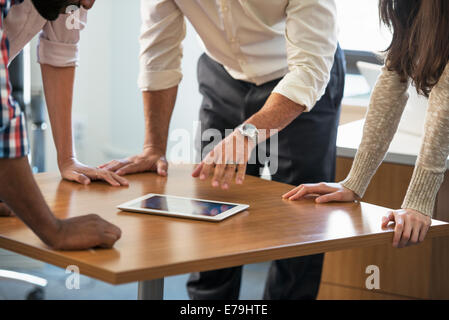 Four people leaning on a table at a meeting, looking at a digital tablet. Stock Photo