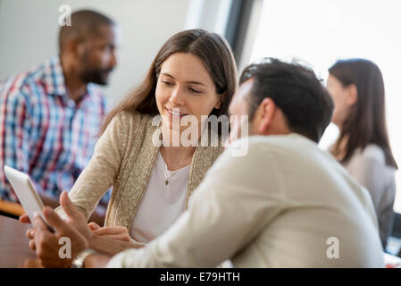 Four people in an office, two men and two women, a couple looking at the screen of a digital tablet. Stock Photo