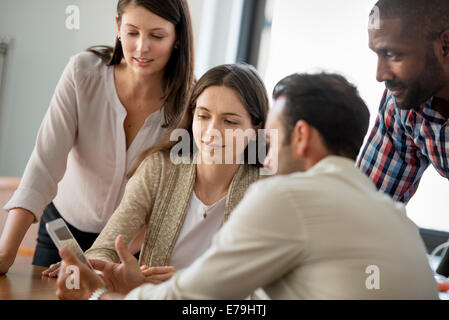 Four people, men and women, grouped around a digital tablet, looking at the screen. Stock Photo