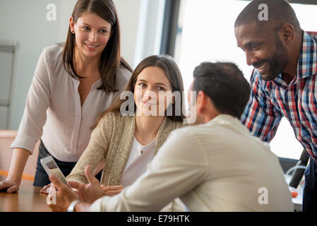 Four people, men and women, grouped around a digital tablet, looking at the screen. Stock Photo
