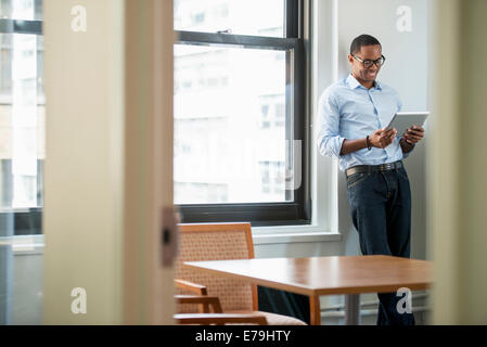 A businessman using a digital tablet, standing by a window. Stock Photo