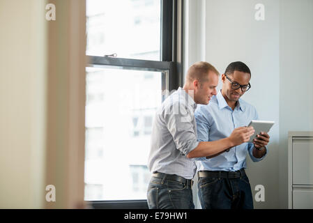 Two men by a window looking at a digital tablet. Stock Photo