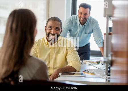 Three people in an office, two men and  a woman with computer monitor and digital tablet. Stock Photo