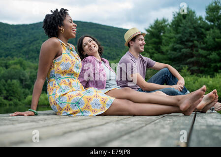 A group of people sitting on a woode pier overlooking a lake. Stock Photo
