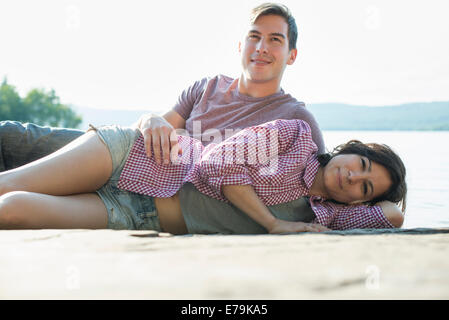 A couple relaxing, lying on a wooden jetty by a lake in summer. Stock Photo