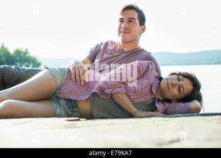 A couple relaxing, lying on a wooden jetty by a lake in summer. Stock Photo