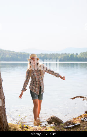 A girl in a straw hat paddling in the shallow waters of a mountain lake. Stock Photo