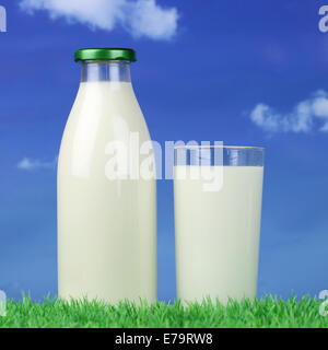 Milk in a bottle and glass on green meadow in front of a blue sky Stock Photo