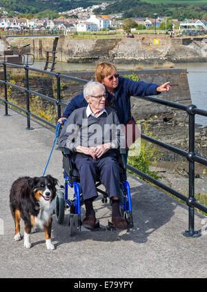 A daughter pointing out the sights of the harbour at Burry Port, Wales, to her elderly disabled father in a wheelchair Stock Photo