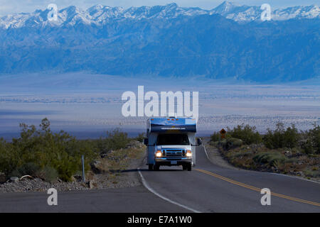 RV on State Route 190 climbing up from Death Valley over Panamint Range, with snowy Grapevine Mountains in background, Death Val Stock Photo