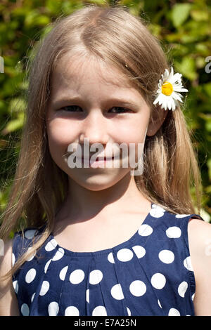 little caucasian girl with camomile flower in long hair stands and smiles on outdoor nature background