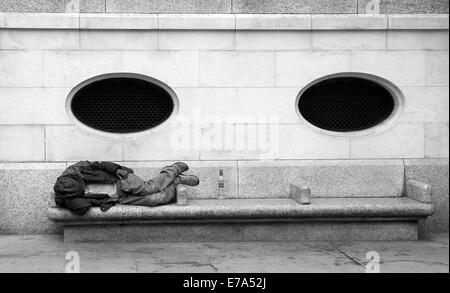 A homeless person asleep on a bench Stock Photo