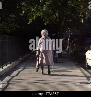 A senior woman using a cane walking on a city sidewalk, rear view Stock Photo