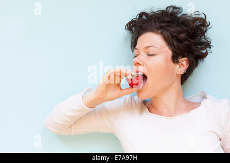 A woman eating strawberry over blue background Stock Photo