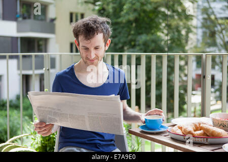 Young man reading newspaper while having breakfast at porch Stock Photo