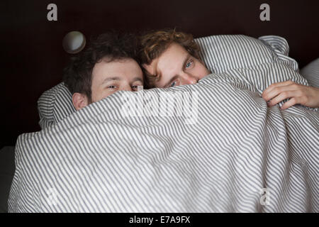 High angle portrait of young gay couple peeking through sheet in bed Stock Photo