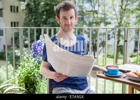 Portrait of young man reading newspaper while having coffee at porch Stock Photo
