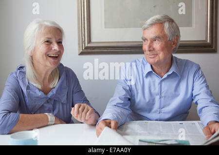 Happy senior couple with newspaper sitting at table in house Stock Photo