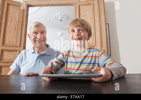 Happy senior man sitting by grandson with digital tablet at home Stock Photo