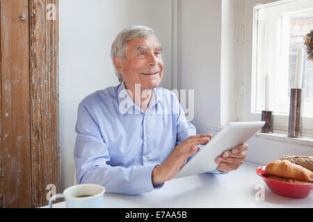Thoughtful senior man looking away while holding digital tablet at table Stock Photo