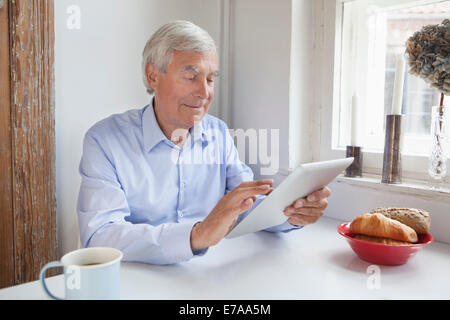 Senior man using digital tablet at breakfast table Stock Photo